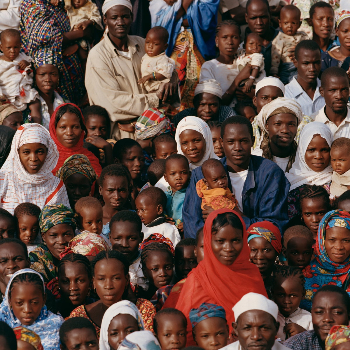 A large gathering of families — parents holding young children — looking toward the camera.