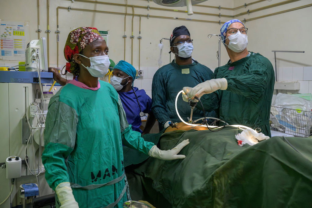 A surgeon and nurses in green gowns care for a patient together in an operating room.