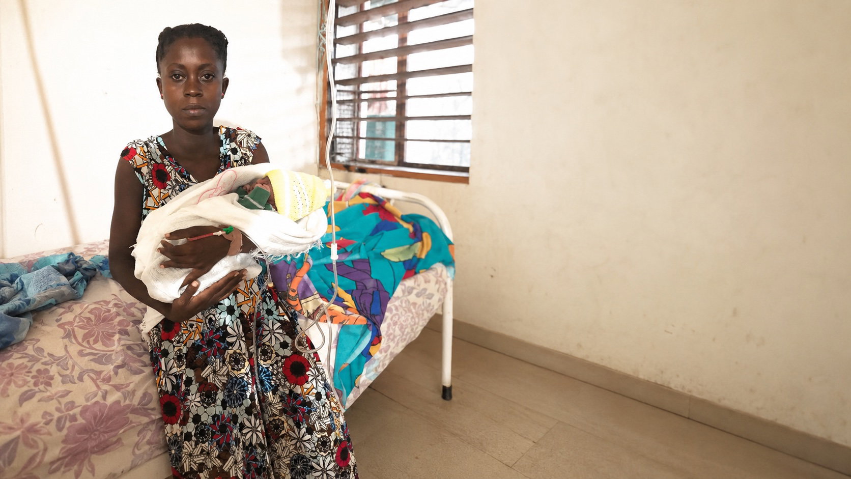 Kymberlie sits on a hospital bed at Hôpital Ste-Croix holding her newborn son wrapped in a blanket.
