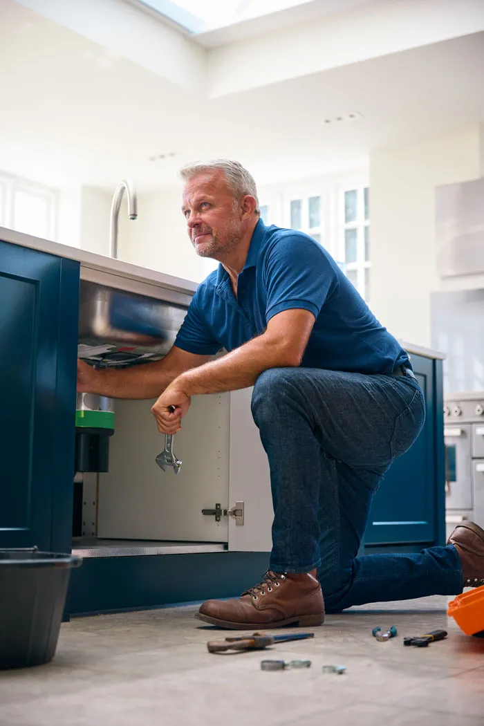 A Repipe & Replumb plumber fixing plumbing under a kitchen sink